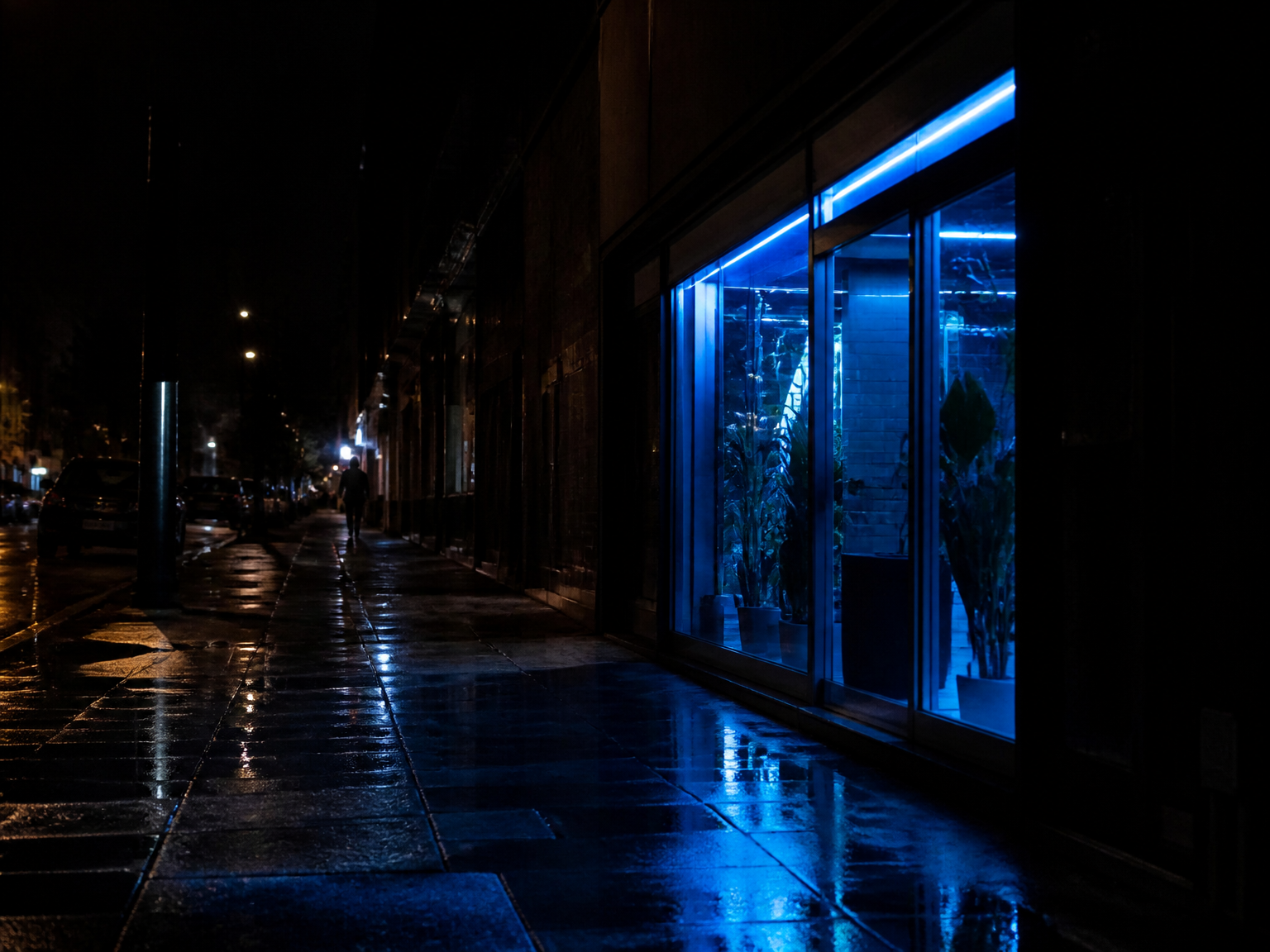A wet night street with blue shop light reflecting on the pavement.