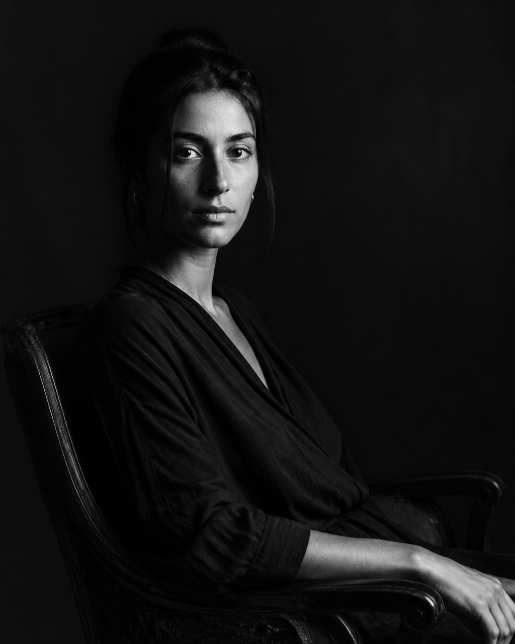 Black and white seated portrait in low light.